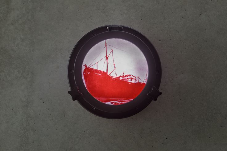 Foto: Blick auf ein rundes Fenster (Bullauge), in dem in leuchtend roter Farbe auf weiß-rosa Hintergrund ein großes Schiff zu sehen ist. Am Bug des Schiffes steht in Großbuchstaben 'Murex'.