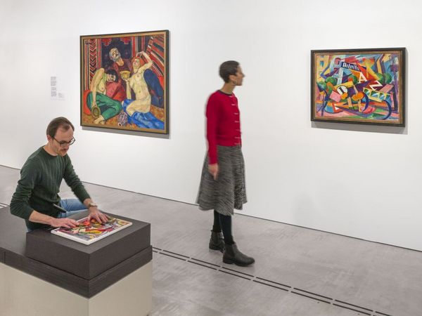 Two people in the exhibition space. One person is touching a tactile model, another is looking at a painting.