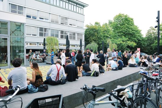 A couple of people are sitting in small groups on a platform outside the museum while chatting.