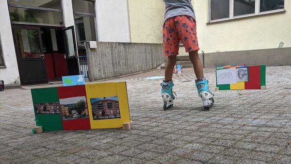 Foto: Kind fährt auf Rolerblades in einem Hof. Daneben kleine, bunte, aufgestellte Pappwände.