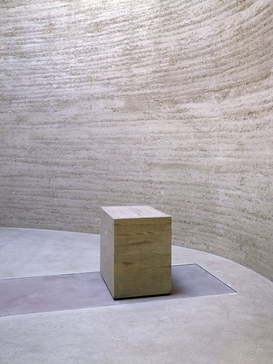 Photo: Interior view of a round, minimalist interior made of clay with a small altar, also made of clay.
