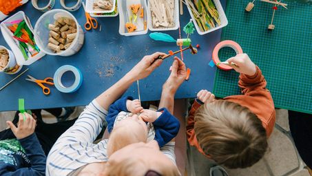 Photo: Adult and two children doing handicrafts together at a table.