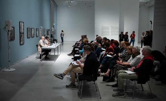 Photo: View of the press conference for the two exhibitions. Many people sit in rows of chairs in front of the two speakers Thomas Köhler and Katia Reich. 