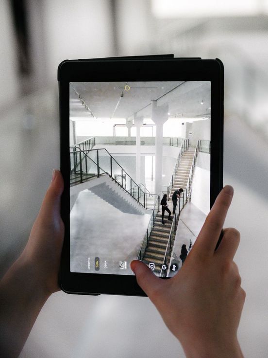 Foto: Person hält ein Tablet in der Hand. Es zeigt die Aufnahme eines Fotos von der Treppe im Museum.