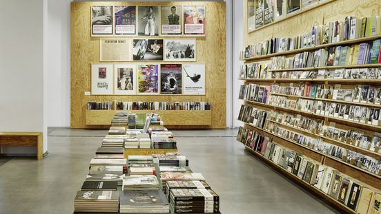 Foto: Im Museumsshop sind Holzregale mit Büchern, Postkarten und anderen Produkte. An der Wand hängen Poster.