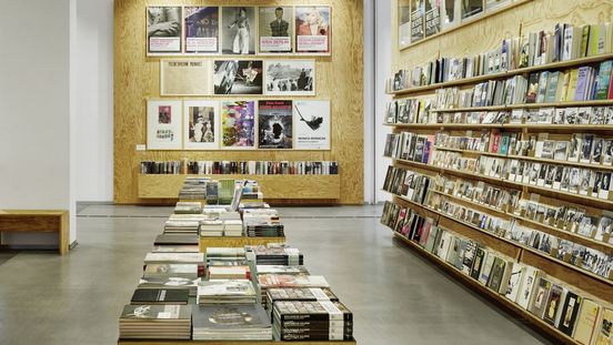 Foto: Im Museumsshop sind Holzregale mit Büchern, Postkarten und anderen Produkte. An der Wand hängen Poster.