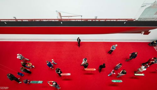 Besucher*innen in der Ausstellung „Monira Al Qadiri. Hero“ Foto: Blick von oben auf viele Menschen in der Monira Al Quadiri-Ausstellung mit leuchtend rotem Teppich und einem großen Öl-Tanker, der an die Wand gemalt ist..