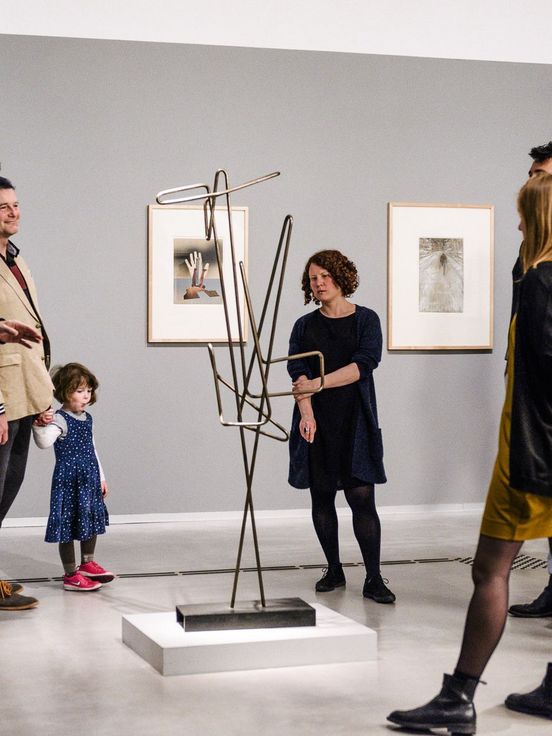 Photo: Adults and a child during a guided tour. They are standing around a sculpture.