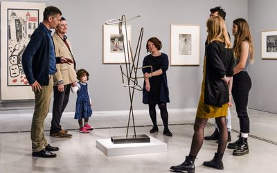 Photo: Adults and a child during a guided tour. They are standing around a sculpture.