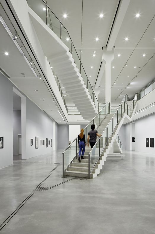 Foto: Zwei Menschen gehen die Treppe hoch. Sie befinden sich in einem zweistöckigen Ausstellungsraum.