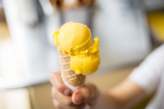 Photo: Close-up of a hand holding a cone of yellow ice cream.
