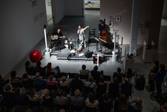 Foto: Die drei Musiker*innen Meret Becker, Yoyo Röhm und Gary Schmalzl auf der Bühne, vor der ein Publikum sitzt.