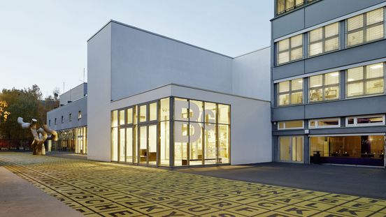 Foto: Gebäude mit Flachdach und Glasfront, auf der das Logo der Berlinischen Galerie abgebildet ist. Davor ein Platz mit einer Metallskulptur und Bodenkunstwerk.