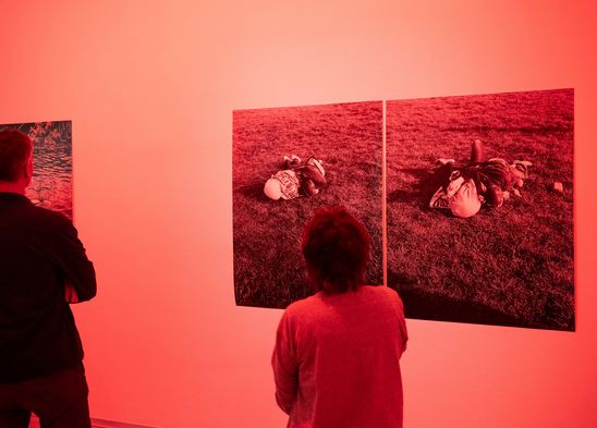 Exhibition view "Özlem Altın. Prisma": Back view of two visitors standing in front of two of the artist's works. The whole picture is bathed in red-orange light.
