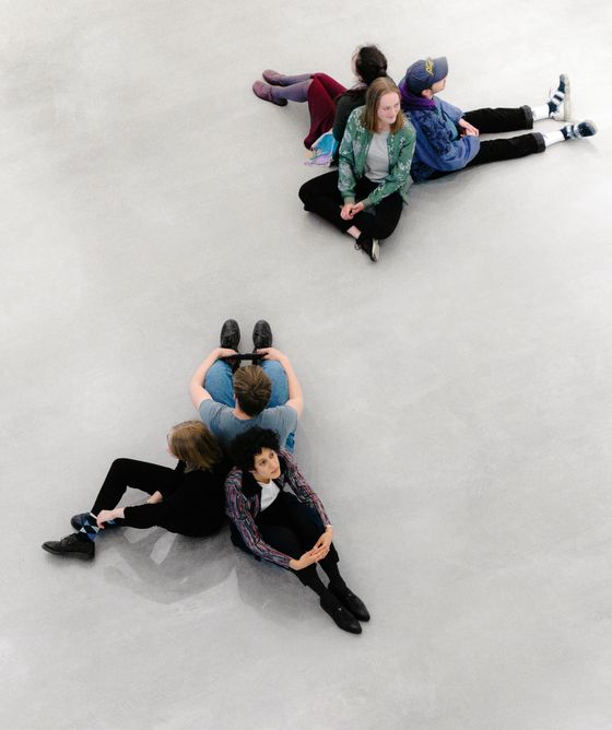 Foto: Junge Besucher:innen sitzen in kleinen Gruppen zusammen auf dem Boden im Museum.