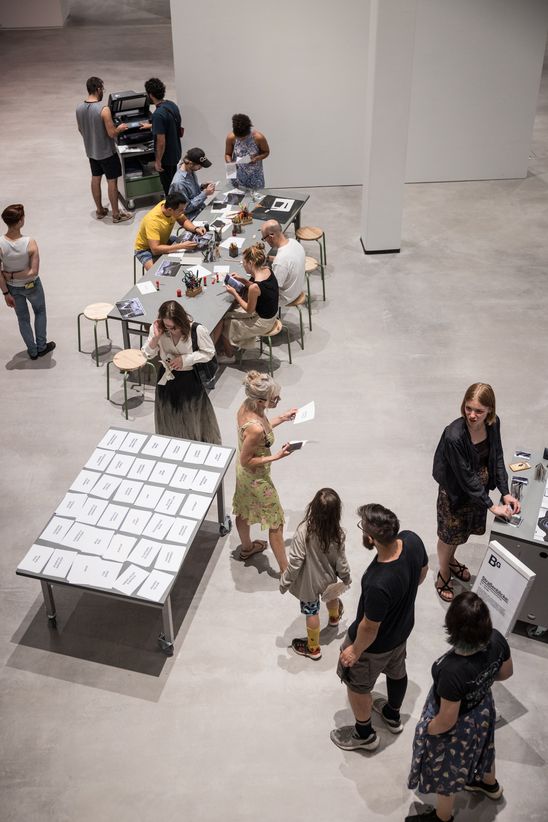 Photo: Some drawing workshop participants stand or sit around two tables and a printer.