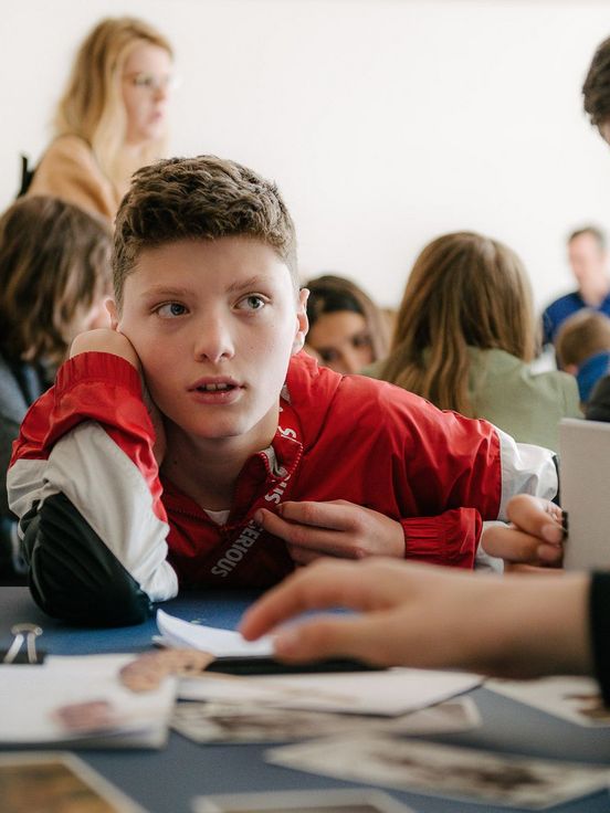 Foto: Schüler*innen sitzen um einen Tisch mit Materialien und diskutieren miteinander