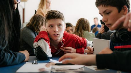 Foto: Schüler*innen sitzen um einen Tisch mit Materialien und diskutieren miteinander