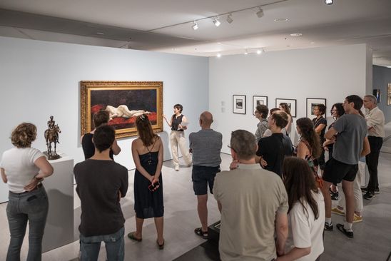 Photo: A large group of people stand in an exhibition space as part of a guided tour.