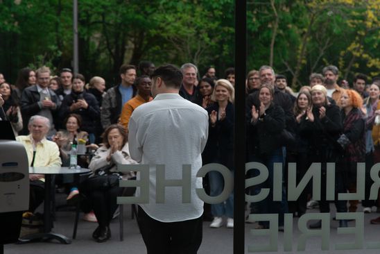 Der Künstler Daniel Hölzl spricht vor einem applaudierenden Publikum im Freien vor der Berlinischen Galerie.
