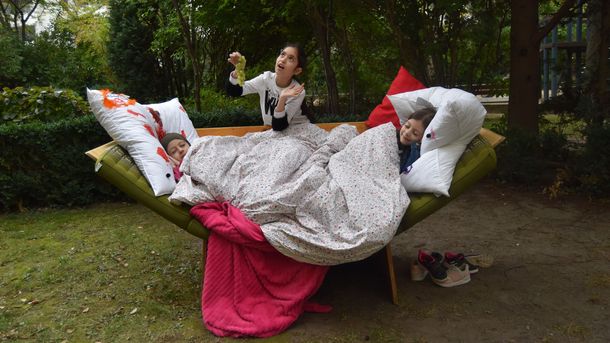 Foto: Kinder liegen und sitzen in einem selbstgebauten Bett im Wald. 