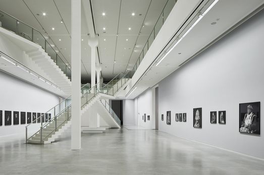 Photo: Two-storey exhibition space with artworks on the walls, two intersecting staircases in the middle.