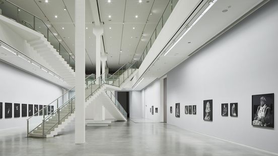 Photo: Two-storey exhibition space with artworks on the walls, two intersecting staircases in the middle.