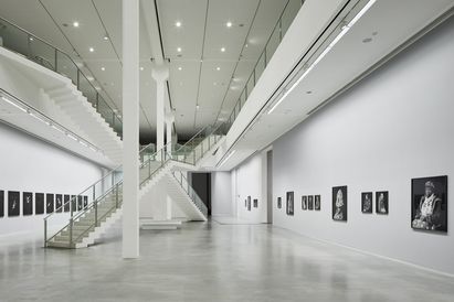 Berlinische Galerie, Foto: © Noshe Foto: Zweistöckiger Ausstellungsraum mit Kunstwerken an den Wänden, in der Mitte zwei sich kreuzende Treppenaufgänge.