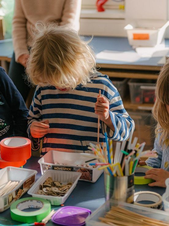 Foto: Drei Kinder spielen mit Bastelmaterialien auf dem Tisch vor ihnen.