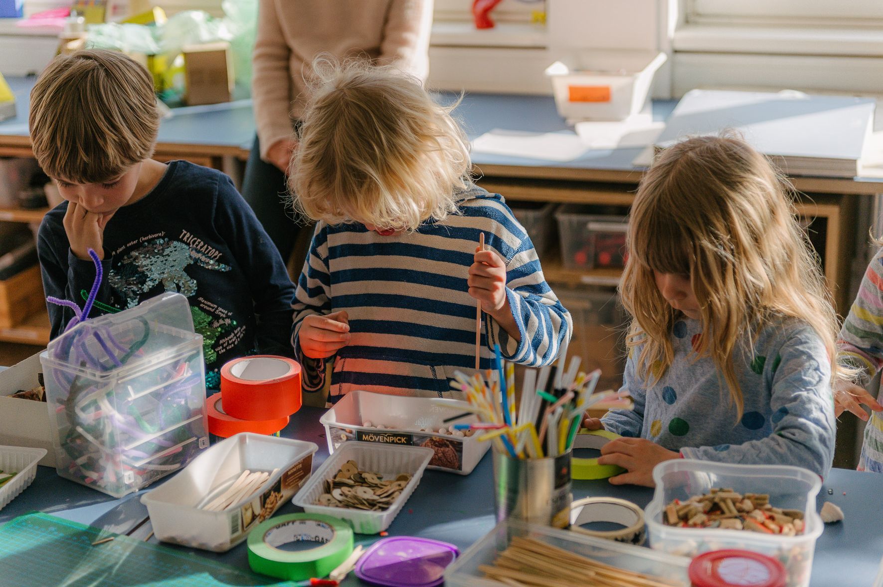 Photo: Three children playing with craft materials on the table in front of them.