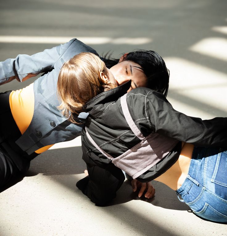 Foto: Zwei Personen liegen einander versetzt gegenüber auf dem Boden in der Sonne. Ihre Münder berühren sich.