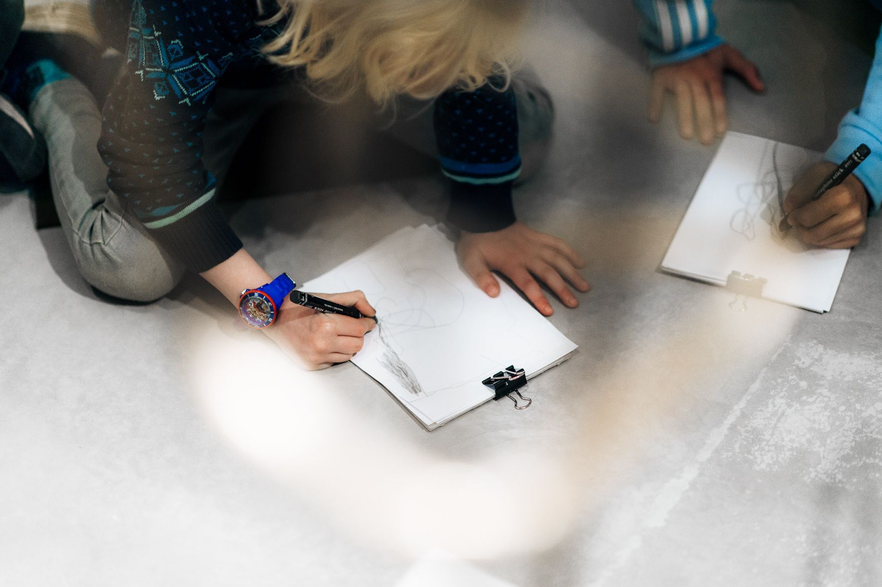 Photo: Two children draw on clipboards on the floor.