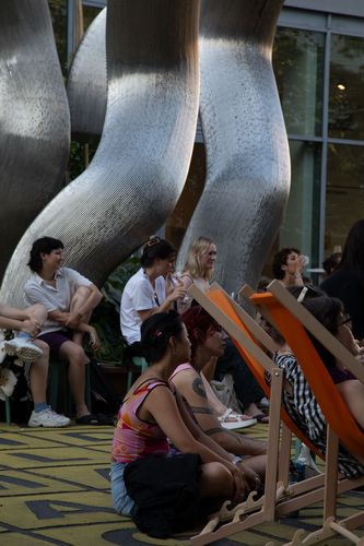 Foto: Seitlicher Blick auf einige Personen, die vor einer großen silbernen Skulptur auf dem Vorplatz der Berlinischen Galerie sitzen.