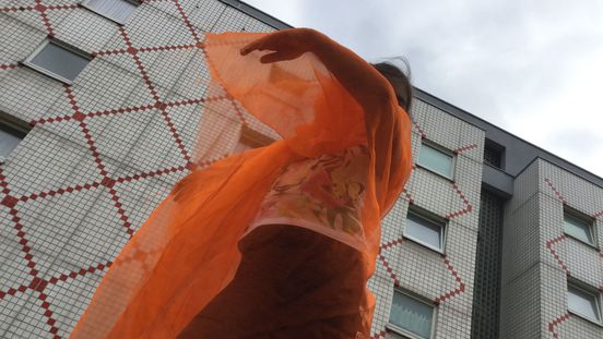 Foto: Ein Kind ist mit halb-transparentem Stoff verhüllt und hat die Arme wie in einer Tanzbewegung erhoben.