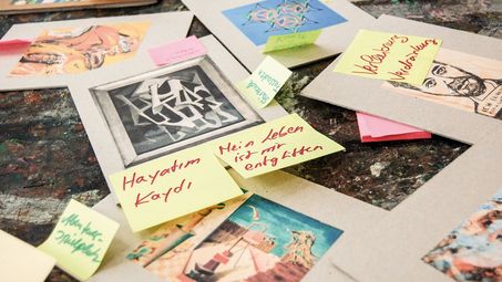 Foto: Ausgedruckte Bilder von Kunstwerken liegen übereinander auf einem Tisch. Auf ihnen sind Post-Its mit Kommentaren angebracht.
