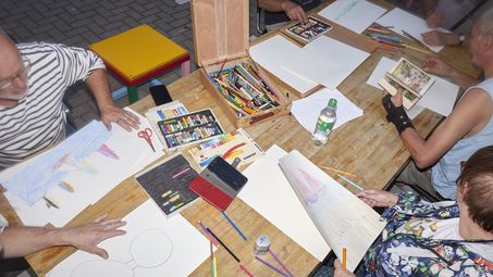 Mehrere Personen sitzen an einem Tisch und malen und basteln