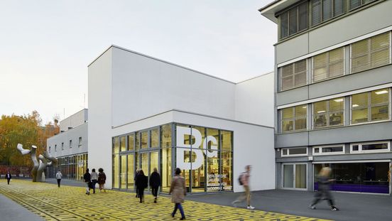 Foto: Gebäude mit Flachdach und Glasfront, auf der das Logo der Berlinischen Galerie abgebildet ist. Davor Menschen auf einem Platz mit Metallskulptur und Bodenkunstwerk.