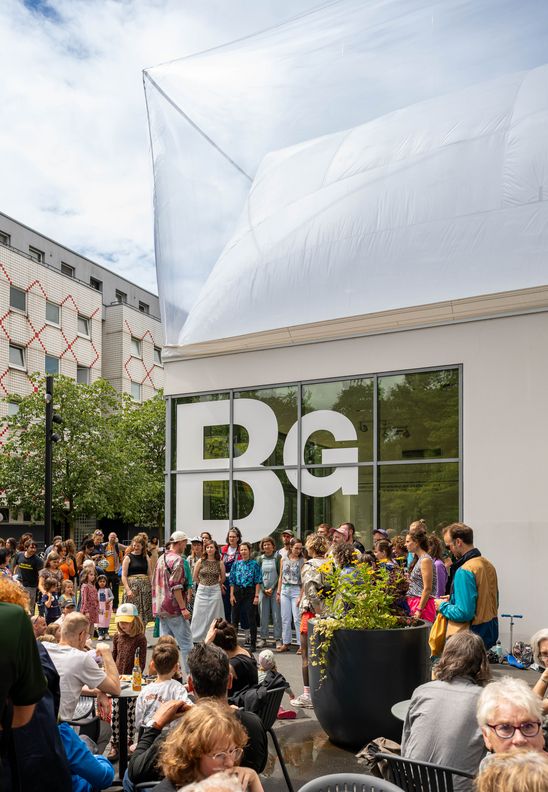 Photo: A group of colourfully dressed people stand in a semi-circle in front of the Berlinische Galerie and sing.