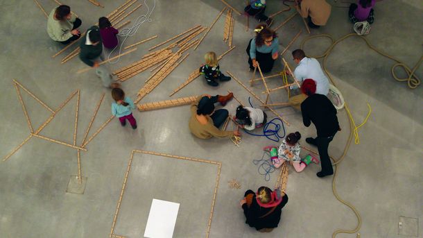 Foto: Erwachsene und Kinder bauen Gebilde aus Holzlatten und Seilen.