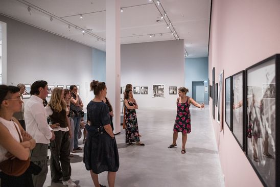 Photo: A large group of people stand in an exhibition space as part of a guided tour.