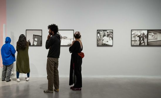 Exhibition view "Akinbode Akinbiyi": View into the exhibition room where four people are standing and looking at black and white photographs by Akinbode Akinbiyi.