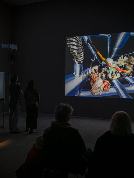 Photo: A few people sit and stand in a video room and look at a large screen.