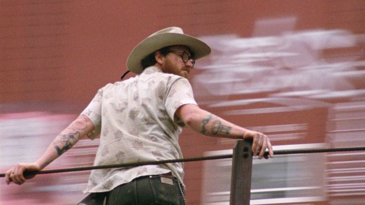 Film still: Rückenansicht einer männlich-gelesenen Person auf einem fahrenden Güterzug.