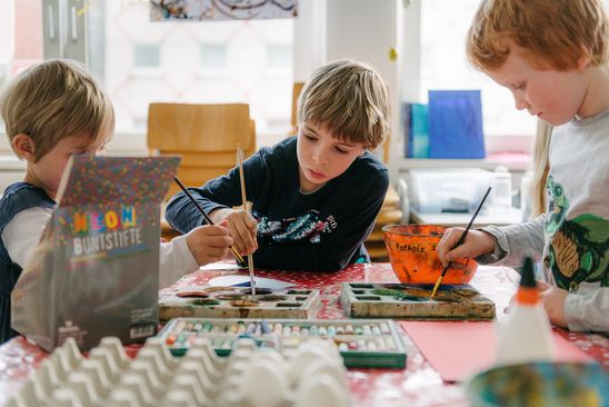 Foto: Drei Kinder malen gemeinsam mit Farbe.