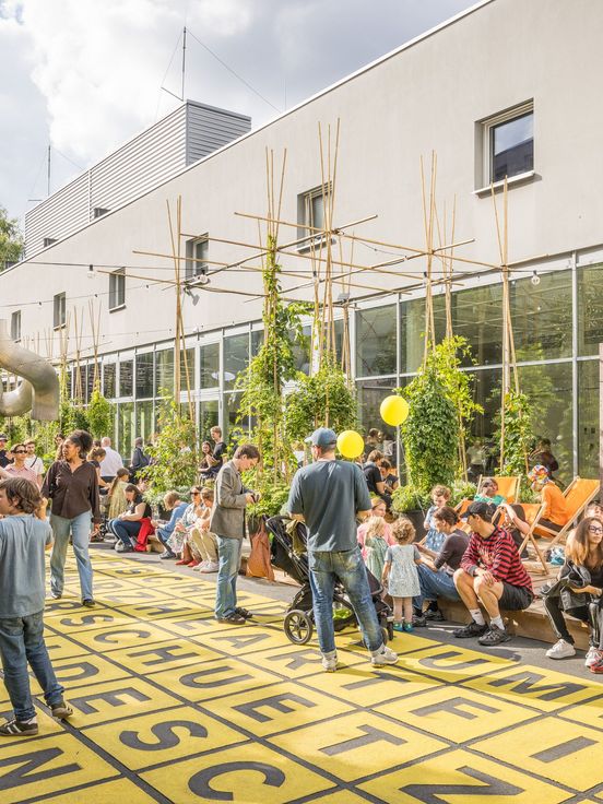 Foto: Seitenansicht der Berlinischen Galerie. Daneben sitzen, stehen oder laufen viele Menschen über den Vorplatz des Museums oder zwischen Pflanzenkübeln, die auf einer Holzplattform neben dem Gebäude platziert sind.