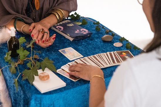 Photo: Two people sit opposite each other at a table with a blue velvet tablecloth. One person lays the cards on the other.