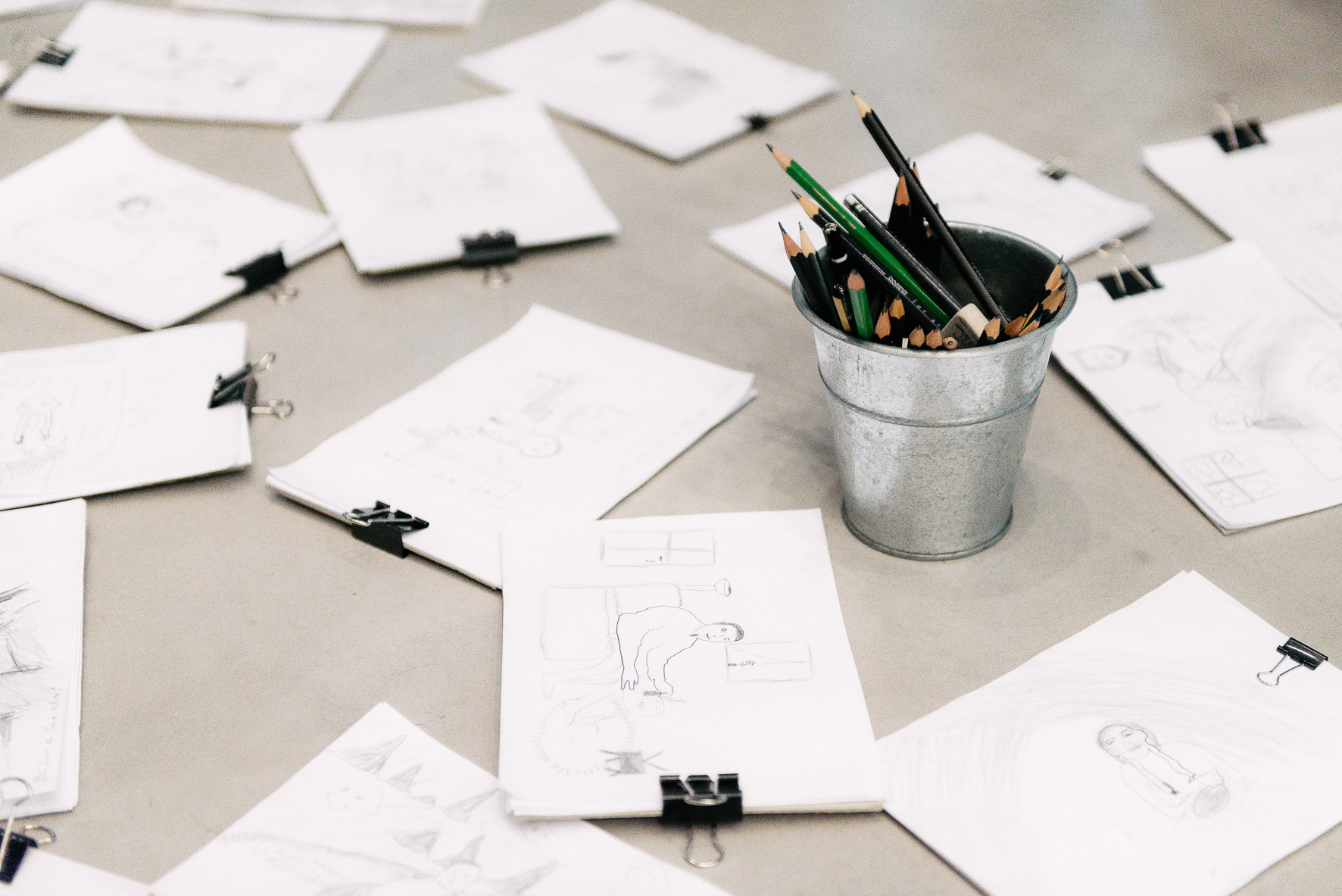 Foto: Auf einem Tisch sind ein Becher mit Bleistiften und Klemmbretter mit Zeichnungen.